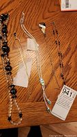 Overview photo showing all five necklaces displayed on a wooden surface including bead necklace, delicate chains with pendants, and chain with iridescent stone pendant.