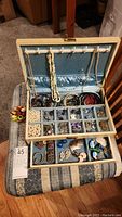 Jewelry box open showing multiple rows of earrings in compartments, various pearl necklaces hanging inside lid, and stacked bangles in bottom section.