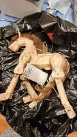 Marionette horse lying partially wrapped in a black plastic bag, showing the side with joints, wear, and tangled strings.