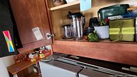 Kitchen shelf with Ninja blender base, multiple blender attachments including pitchers and blending cups, and various kitchen items stored nearby