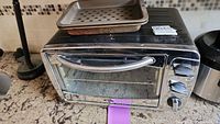 Full view of Oster toaster oven on counter with perforated baking tray on top.