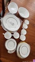 Photo of stacked plates, bowls, cups and saucers showing the entire set for six, highlighting the white bone china with embossed Echo pattern and silver/platinum trim on rims.