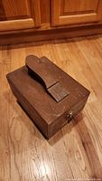 Wooden shoe shine box with handle, latch, and label on the front, sitting on hardwood floor.