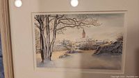 Framed watercolor artwork showing a winter landscape scene with trees and buildings in the background.