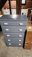 Front view of small blue painted 5-drawer chest showing white drawer handles and surface wear.