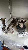 Overall view of two candlesticks, bud vase, julep cup and silver cleaner jar on shelf