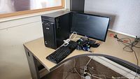 Photo showing an Acer desktop PC tower, monitor, keyboard, mouse, and cables arranged on a wooden table.