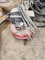 Photo showing a dusty Porter-Cable portable air compressor, red tank, black motor housing, 135 PSI label, air hose coiled on top with pressure gauge visible.