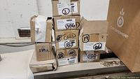 Photo of stacked cardboard boxes labeled with various product codes and handles/knobs references.