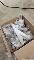 Box filled with multiple plastic bags containing white and metallic silver cabinet door handles and knobs in original packaging.