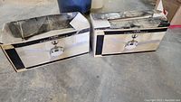 Two boxed Hunter Calibre 48" ceiling fans, shown side by side on a concrete floor, boxes show signs of wear and tear.