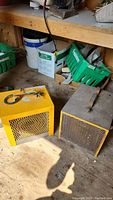 Photo shows two yellow construction heaters on wooden floor with shelves and other tools in background.