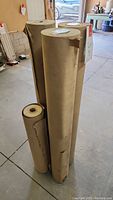Four rolls of brown kraft paper standing upright on a concrete floor in a garage or workshop space.