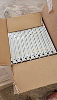 Opened box showing neatly stacked white metal drawer slides with multiple mounting holes.