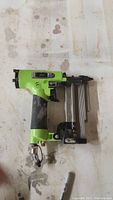 Photo of a Grex 23 gauge pin nailer showing the green body, metallic nail magazine, black grip and air hose connector.