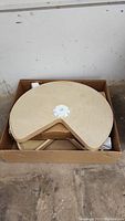 Photo showing the maple wood lazy Susan inside a cardboard box. The lazy Susan is circular with a white central rotating mechanism.