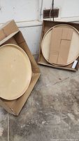 Two maple laminated plywood lazy susan turntable kits in original boxes on concrete floor.