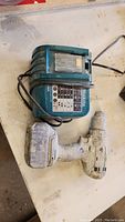 Photo showing a white cordless Makita drill with battery attached next to a blue Makita charger unit with power cord.