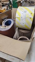 Box containing multiple rolls of sandpaper assorted by type and grit.