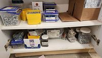 View of cabinet shelves containing multiple containers with screws and fasteners in assorted bins, boxes, and jars.
