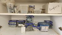 View of cabinet shelves containing multiple plastic containers and cardboard boxes filled with screws, fasteners, and hardware items.