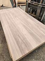 Photo showing one large rectangular sheet of walnut veneered particle board with visible wood grain pattern. Person standing near the sheet for scale.