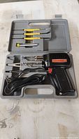 Electric soldering iron set in molded plastic case showing pistol grip iron, multiple tips, four yellow-handled screwdrivers, and metal tool.