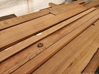 Solid lumber boards of various thicknesses stacked together, showing grain and a few knots.