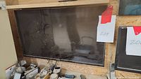 Flat-screen TV mounted on a wall panel, dusty screen, remote control visible, wall mount present