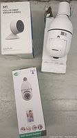 Three smart cameras: two Laxihub M1 boxes and one WiFi Smart Camera bulb-style box with one camera partially unpacked.