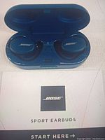Bose Sport Earbuds inside the open charging case with Bose Sport Earbuds quick start guide booklet under the case.