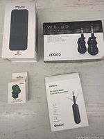 Four boxed guitar accessory items: MeloAudio Exp 001 foot pedal, Lekato WS-50 wireless guitar system box, Morin AF-107 tuner box, Ugreen Bluetooth audio receiver/transmitter box on white surface.