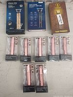 Lot of hair clippers and facial hair removers arranged on a flat surface showing brand names and packaging.