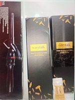 Two boxed WavyTalk Nano-Titanium flat irons and small sealed bottle of SN Hair Wax on a white surface, boxes black with gold accents.