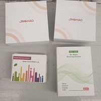 Four hearing amplifier units with factory packaging, showing branded boxes and product boxes.