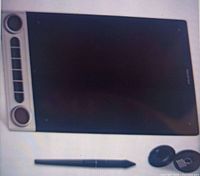 Black Huion Inspiroy Dial 2 wireless drawing tablet with shortcut buttons and dials, stylus pen and pen stand on a light background.