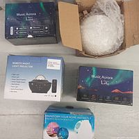 Four projector lamps and one remote night light projector in original factory packaging placed on a floor.