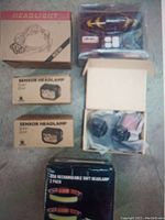 Photo showing all six items packaged on floor: one large headlamp box, two sensor headlamp boxes, 1 black USB rechargeable soft headlamp box, pair of yellow arrow signal tail lamps in plastic packaging.