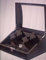 Open black double watch winder with glass lid, showing two cushioned watch holders inside and a silver control knob.