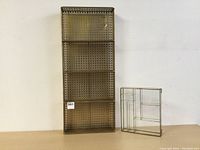 Two brass ornamental shelves side by side on a wooden surface against a neutral wall: a large rectangular brass shelf with geometric perforations, and a smaller rectangular brass and glass shelf.