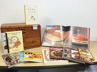 Wood bread box with shelf and a variety of cookbooks and recipe books arranged on a table