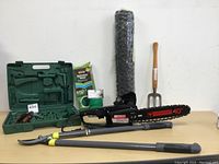 Full view of all items on table including electric chain saw, pruning kit, garden fork, poultry netting, sprinkler hose, and rubber coated flex tire