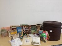 Photo showing vintage vinyl hassock and assortment of needlecraft books, kits, and supplies on table.
