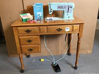 Singer sewing machine set into wooden cabinet showing machine and cabinet drawers with foot pedal on floor.