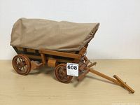 Side view of vintage wooden covered wagon lamp with fabric cover, showing wooden wheels and tongue.