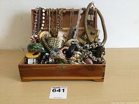 Overview of open wooden jewelry box filled with assorted necklaces, bracelets, rings, pins and hair accessories.