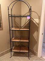Full view of the black metal baker's rack standing against beige walls and floor, showing all four tile shelves.