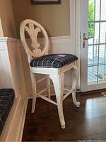 Full view of one painted wooden barstool showing white carved frame and black plaid upholstered seat.