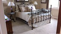 Full view of queen sized metal bed frame with comforter set and decorative pillows on bed.