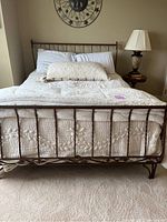Front view of metal queen sized bed frame made of twisted metal bars with quilted light-colored comforter and pillows.